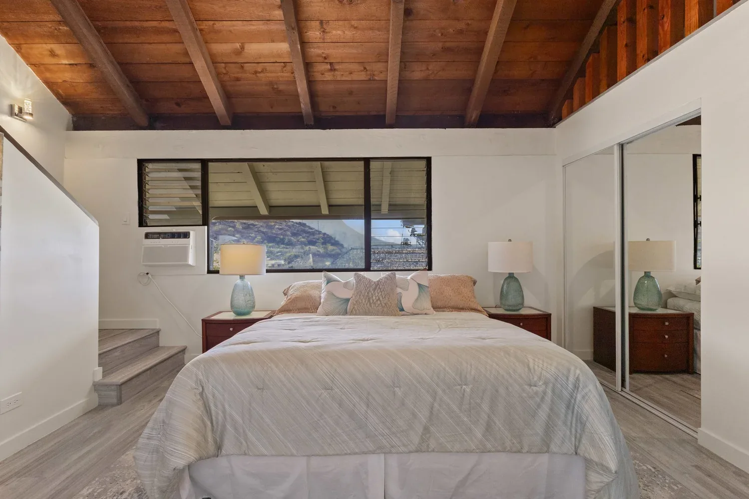 A bedroom with a large bed, nightstands with lamps, a window with a mountain view, and mirrored closet doors.
