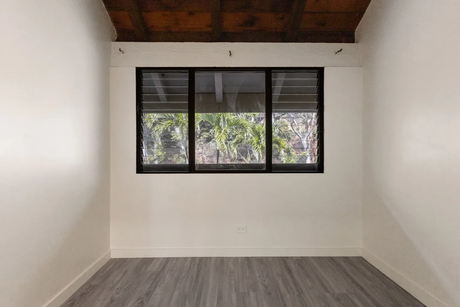 Bedroom with white walls, a large window, and wooden ceiling.